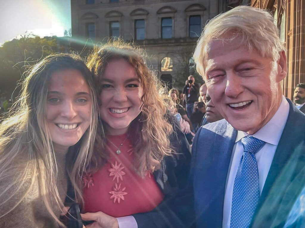 Two young woman shake hands with Bill Clinton